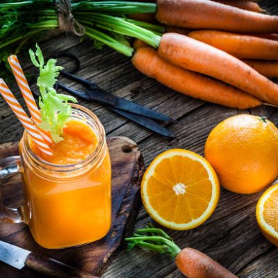 Healthy drink: high angle view of a drinking glass filled with fresh organic orange and carrot juice shot on rustic wooden kitchen table. Whole and sliced oranges and carrots are all around the glass. A kitchen knife and kitchen scissors complete the composition. Predominant colors are orange, green and brown. Low key DSRL studio photo taken with Canon EOS 5D Mk II and Canon EF 100mm f/2.8L Macro IS USM.